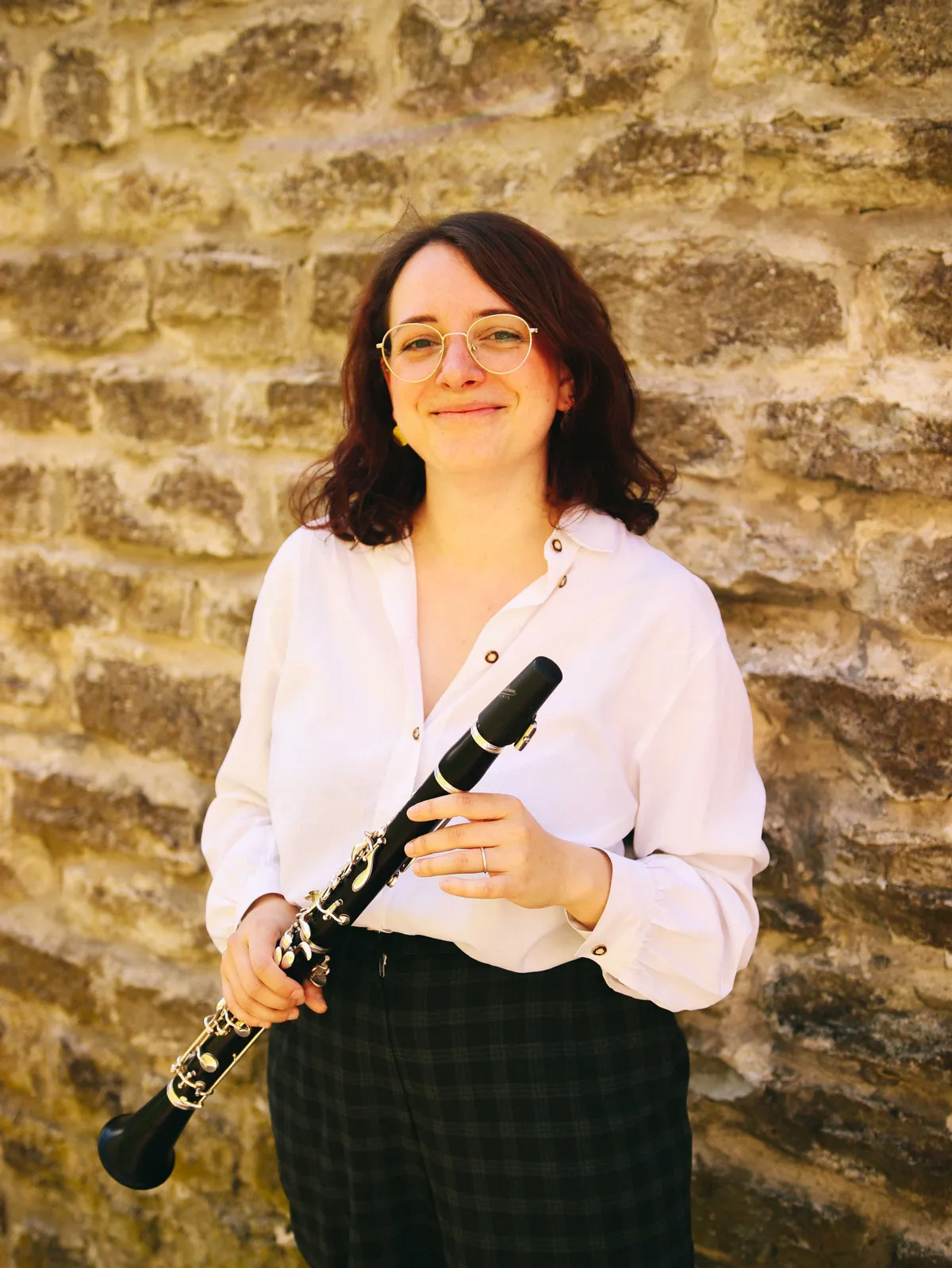 Vittoria Ecclesia sorride tenendo un clarinetto, davanti a un muro di pietra
